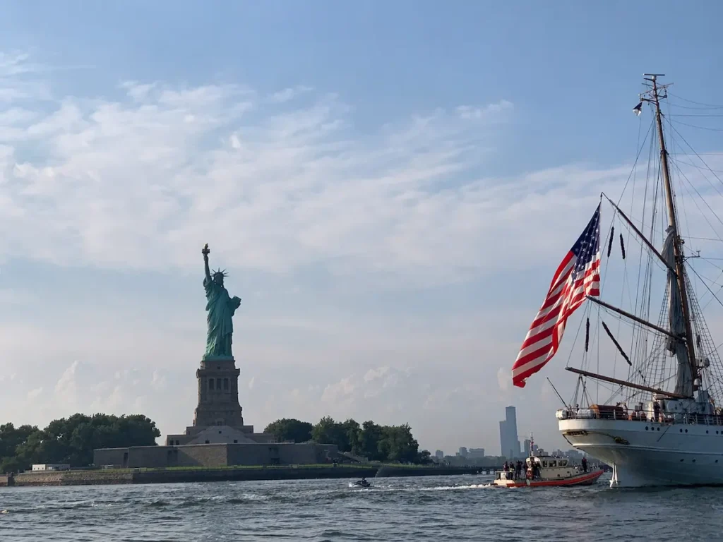 ニューヨークの自由の女神をフェリーから見る風景 海と船とアメリカ国旗が見える観光シーン